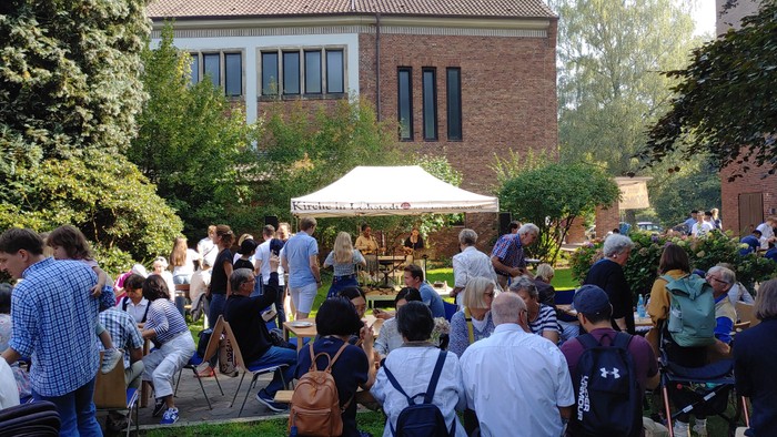 Bühne an der Christ-König-Kirche mit vielen Menschen drum herum an Tischen