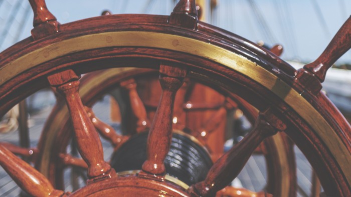 Steuerrad eines Segelschiffs mit Mast im Hintergrund