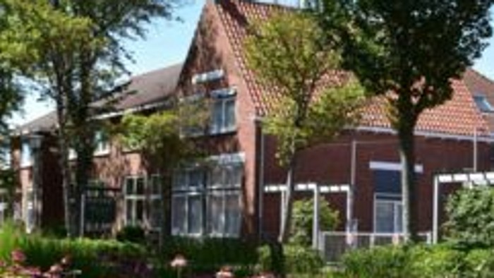 Modernes Ziegelgebäude mit großen Fenstern, umgeben von einem lebendigen Garten und üppigen grünen Bäumen.