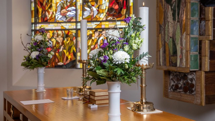 Elegant alteropsætning med blomsterarrangementer, lys og religiøst farvet glas i en rolig kapel.
