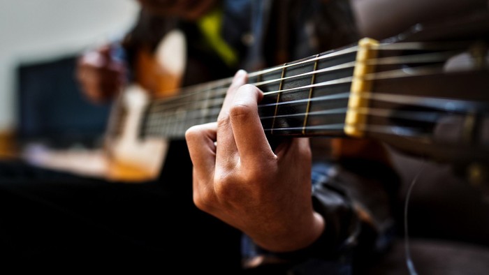 En person, der spiller på en akustisk guitar med præcis håndplacering på gribebrættet.