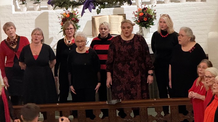 En gruppe kvinder i kor dragter står sammen i en pyntet kirke, enten i gang med at synge eller posere til et foto.
