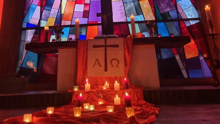 Buntes Kirchenfenster aus Glas erhellt einen friedvollen Altar, der mit Kerzen und einem Kreuzsymbol geschmückt ist.