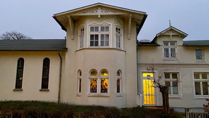 Das Bild zeigt ein zweistöckiges Haus mit einem Erker und einem gelben Tor.