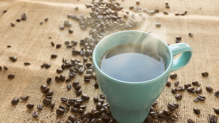 En lille blå tekopper med mælkekaffe og kaffebønner på bordet