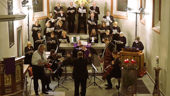 Ein Chor und ein Orchester treten gemeinsam in einer prächtigen Kirche während eines festlichen Konzerts auf.