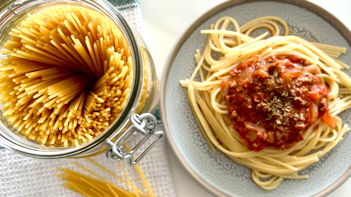Frisk spaghetti i et glas med kogt pasta og tomatsauce på en tallerken ved siden af.