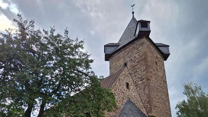 Historischer Backsteinturm mit üppigem Grün und weißen Blumen in einer ruhigen, bewölkten Umgebung.