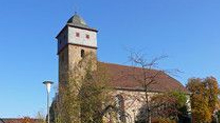 Historische Kirche mit hohem Glockenturm vor klarem blauem Himmel und herbstlichem Laub.