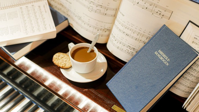En kop kaffe og en kage på skrivebord med noter og bog