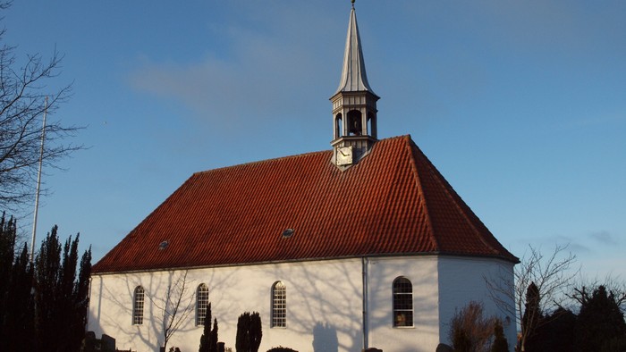 En hvid kirke med rødt tag og tårn mod en klar blå himmel