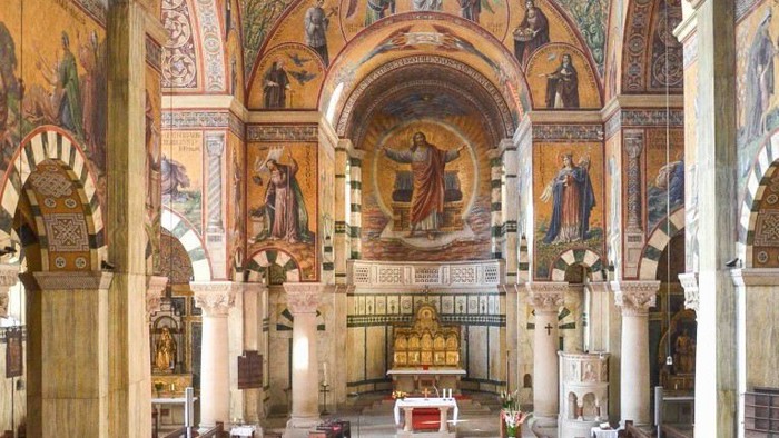 Innenraum einer Kirche mit Säulen, Mosaiken und Kirchenbänken