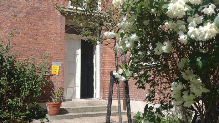 Ein charmanter Ziegegebäude-Eingang, geschmückt mit blühenden weißen Blumen und üppigem Grün.