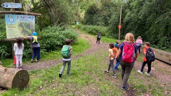 Kinder und Erwachsene gehen auf einem Waldweg.