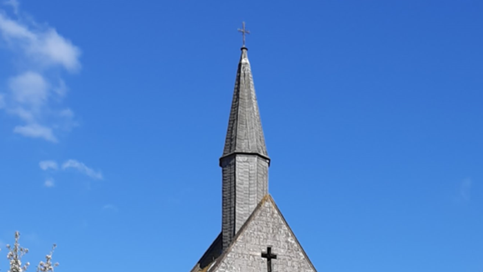 Kirche mit Wiese davor, blühendem Kirschbaum links und blauem Himmel