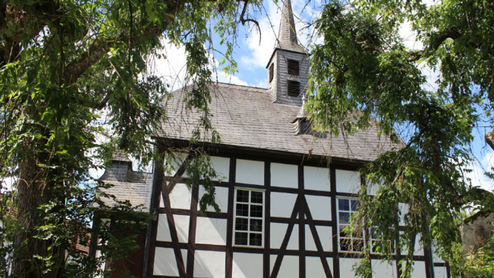 Historisches Gebäude mit Fachwerk, Steinsockel und Glockenturm.