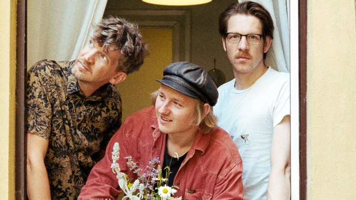 Vier Personen, die gemeinsam in einem Türrahmen stehen und Blumen halten, lächeln herzlich.