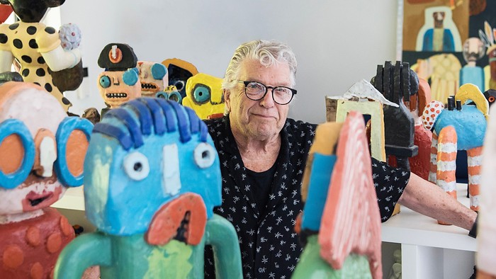 En kunstner poserer stolt mellem sine farverige, fantasifulde keramiske skulpturer i et atelier.
