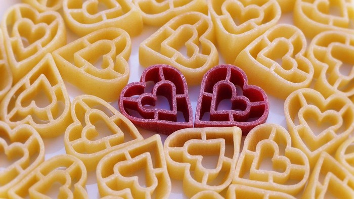 Hjerteformede pastastykker omgivet af traditionel fusilli-pasta med to røde hjerter i midten.