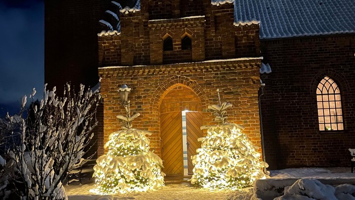 En lyssatte juldekoration foran en middelalderlig kirke.
