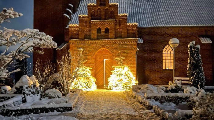 En kirke belyset ved natten med julelygter og sne.