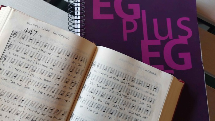 Das Foto zeigt eine aufgeschlagene Seite des Evangelischen Gesangbuchs und die Titelseite des EG+