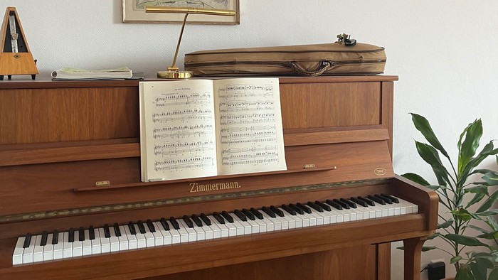 Elegantes Holzklavier mit Notenblättern, gerahmten Kunstwerken und einer kleinen Topfpflanze in der Nähe.