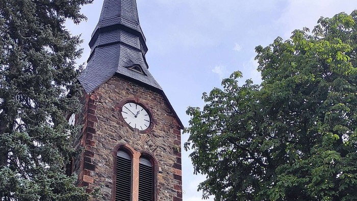Alte Kirche mit hohem Turm und Uhr, umgeben von Bäumen