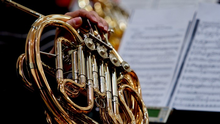En person spiller horn i et orkester.