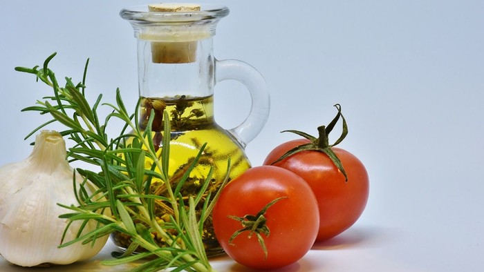 Das Bild zeigt eine Glasflasche mit Öl, Knoblauch, Rosmarin und Tomaten
