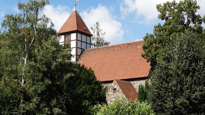 Ein rotes Dachhaus mit Turm zwischen Bäumen.