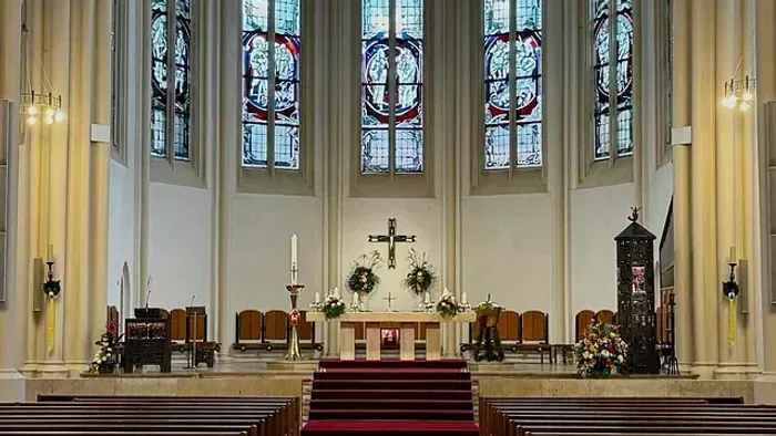 Elegante Kircheninnenausstattung mit hohen Buntglasfenstern und einem ruhigen Altar mit hölzernen Kirchenbänken.