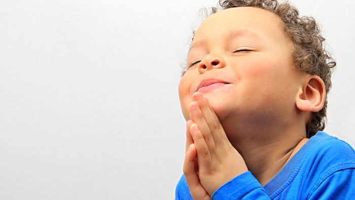 Enfant souriant, main sur la bouche, vêtu de bleu.