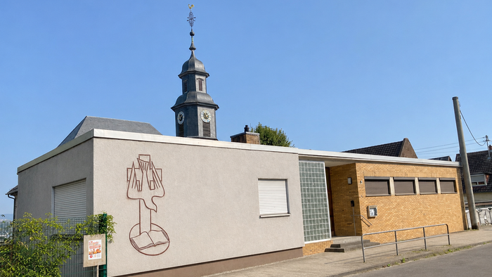 Flachdachgebäude mit Kirchturm im Hintergrund.