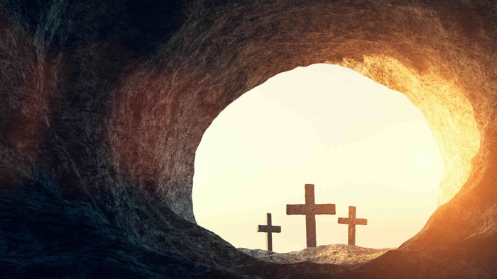 Trois croix devant une ouverture rocheuse éclairée par le soleil.
