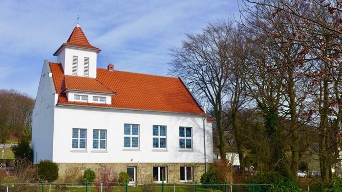 Ein charmantes weißes Gebäude mit rotem Ziegeldach und kleinem Turm, umgeben von kahlen Bäumen.