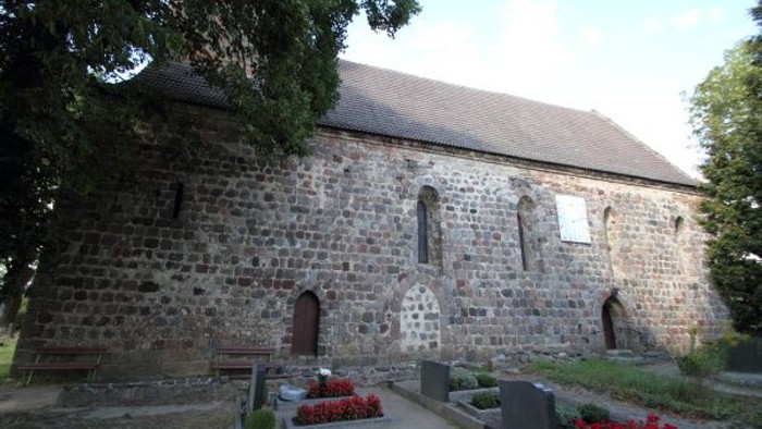 Historische Steinkirche mit Grabsteinen und farbenfrohen Blumenarrangements in einer ruhigen Friedhofsatmosphäre.