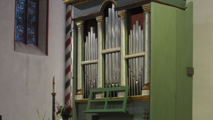 Eine traditionelle Kirchenorgel mit einem hölzernen Lesepult und einem Blumengesteck auf einem erhöhten Podest.