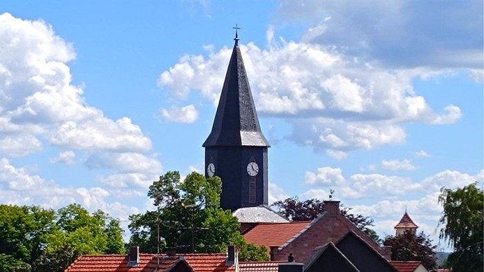 Kirchturm mit Uhrwerk vor blauem Himmel und weißen Wolken