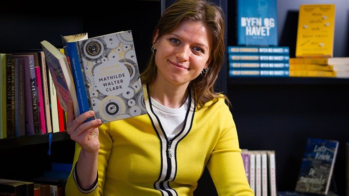 Kvinde i gult trøje holder op med bog i bibliotek