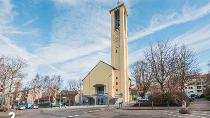 Eine helle Kirche mit Turm steht in einer Umgebung mit Bäumen.