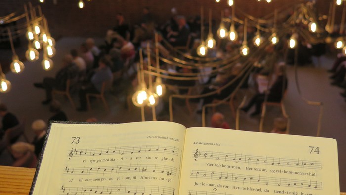 Kor, der synger i en festligt oplyst kirke med salmebøger åbne på noderne.