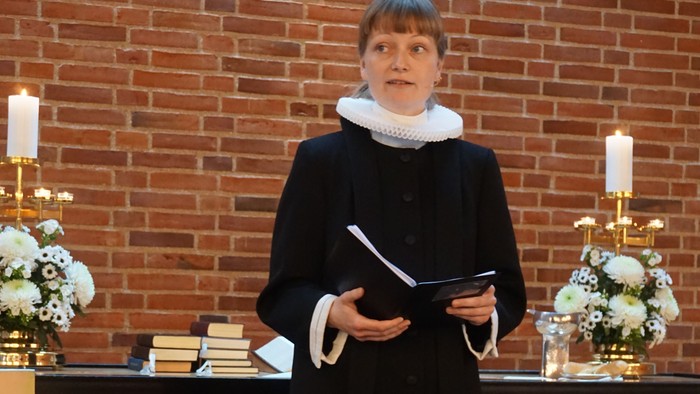 En præst står i kirke med bog og kæmp.