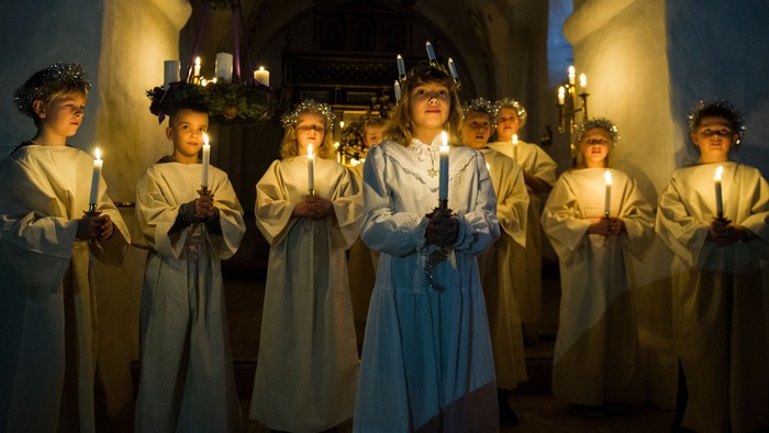 En gruppe kvinder i hvide kler og kranser holder lys i en kirke.