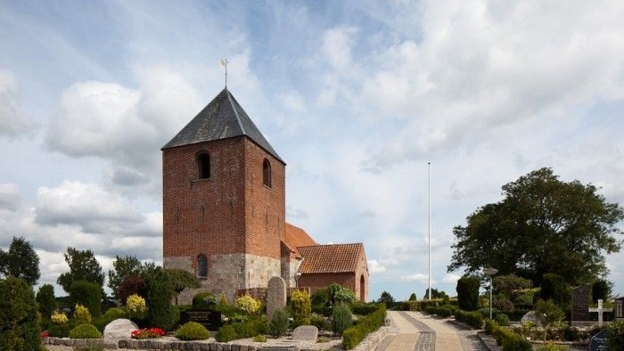 En smuk kirke med tårn og spiret, omgivet af træer og en sti.