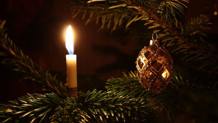 En lysende lykt mellem grønne grenar og et glasornament.