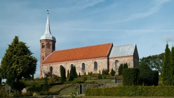En rød kirke med spiret og klokketårn op mod et blåt himmel.