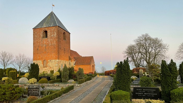 En gammel kirke med tårn og røde tag, omgivet af en park med buske og steder.
