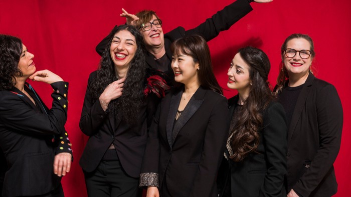 Un groupe joyeux de femmes en tenue noire posant avec entrain devant un fond rouge.