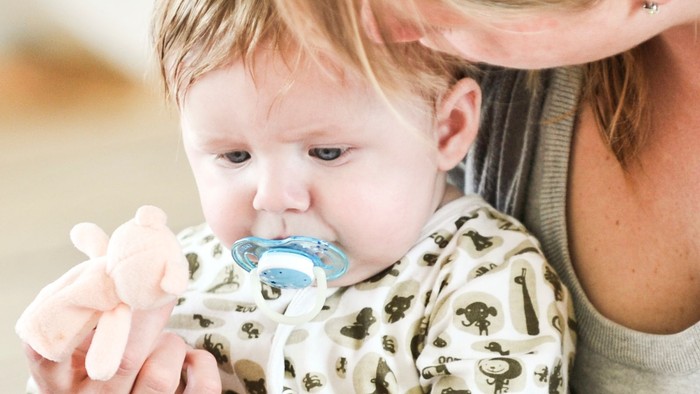 En kvinde holder en baby, som leger med en tøjdyr og en sut.